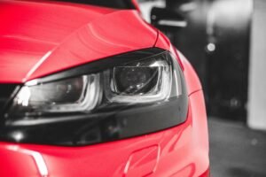Closeup of shiny plastic headlight of red tuned automobile parked in underground garage