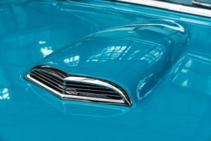 Detailed view of a blue vintage car hood featuring chrome accents, reflecting indoor lighting.