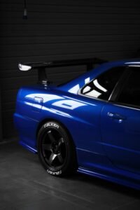 Close-up of a blue Nissan Skyline R34 GT-R showcasing a prominent spoiler, indoors.
